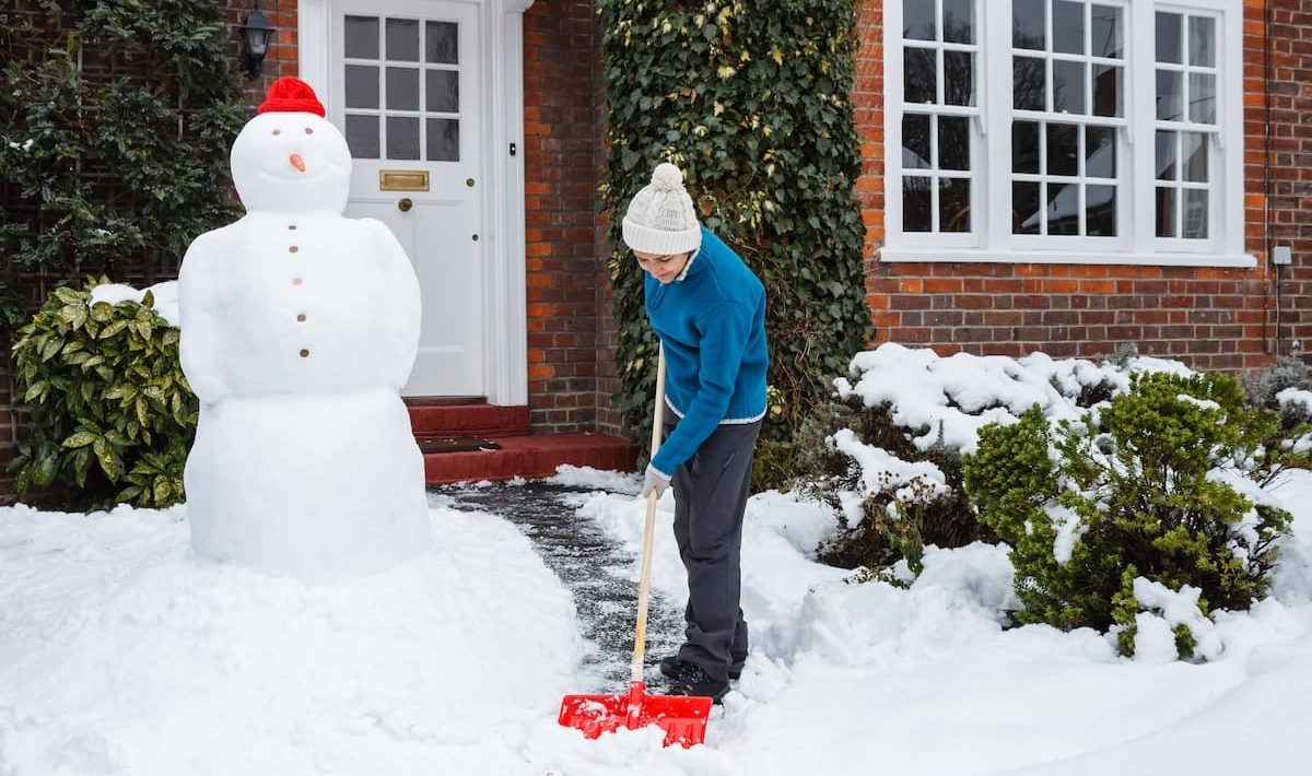 een vrouw ruimt sneeuw van de weg en de trap